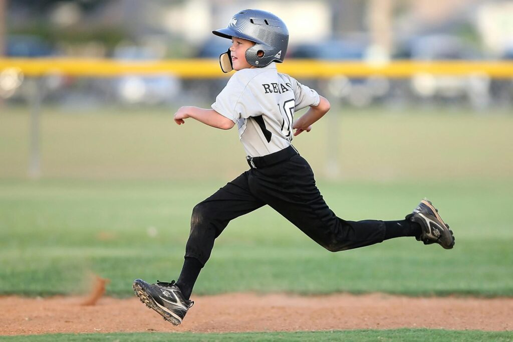 Action shot of a young baseball player running fast on the field, wearing uniform and helmet.